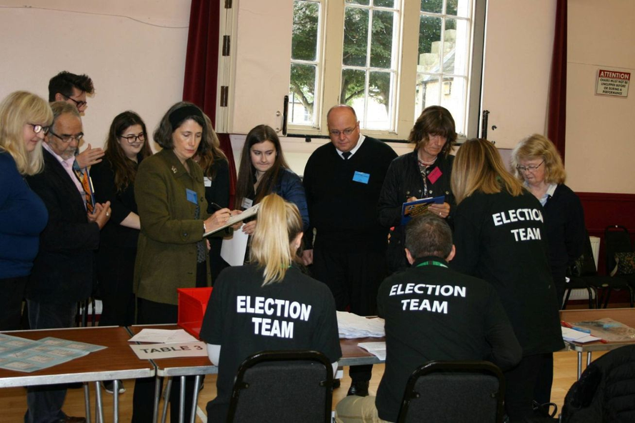 A group of candidates look on apprehensively as an election team prepares to count ballot papers.